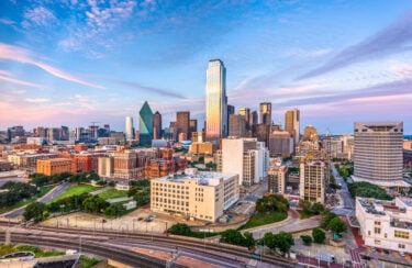 Jet Charter Aerial view of downtown Dallas at sunset, showcasing its skyline with prominent buildings under a colorful sky, ideal for viewing from a private jet charter. Jetvia