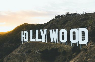 Jet Charter The Hollywood sign, situated on a hillside under a golden sunset sky, is complemented by lush greenery surrounding the iconic white letters, often admired during private jet charter flights. Jetvia