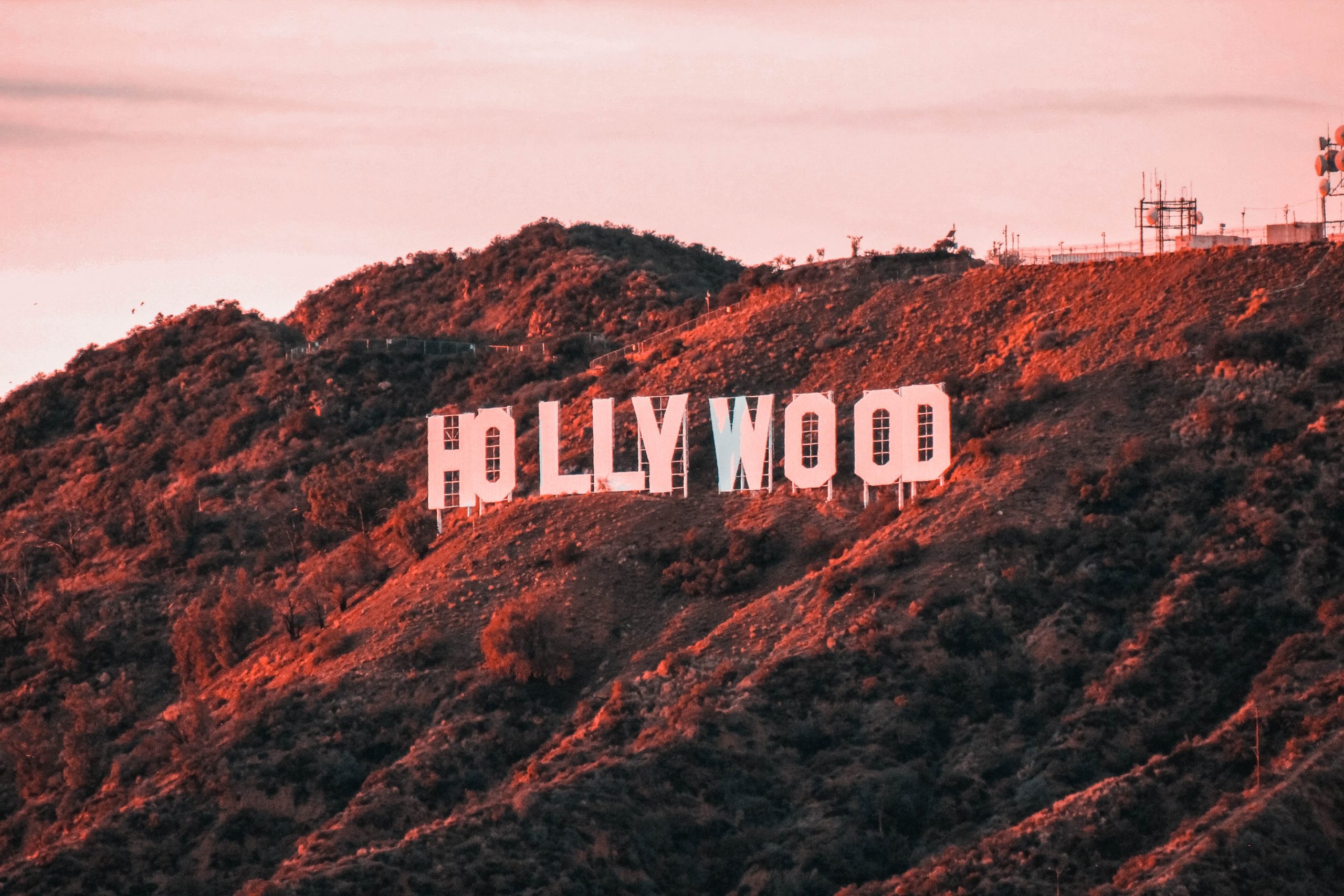 Jet Charter The iconic Hollywood sign on a hillside, bathed in a pinkish hue from the setting sun, with lush greenery and a clear sky in the background, often seen by travelers on private jet charters. Jetvia