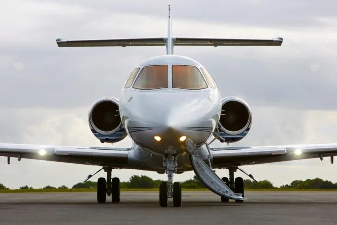 Jet Charter A Private Jet Charter is positioned on a runway, facing forward, with its engines visible and landing lights on, against a backdrop of a cloudy sky at dawn or dusk. Jetvia