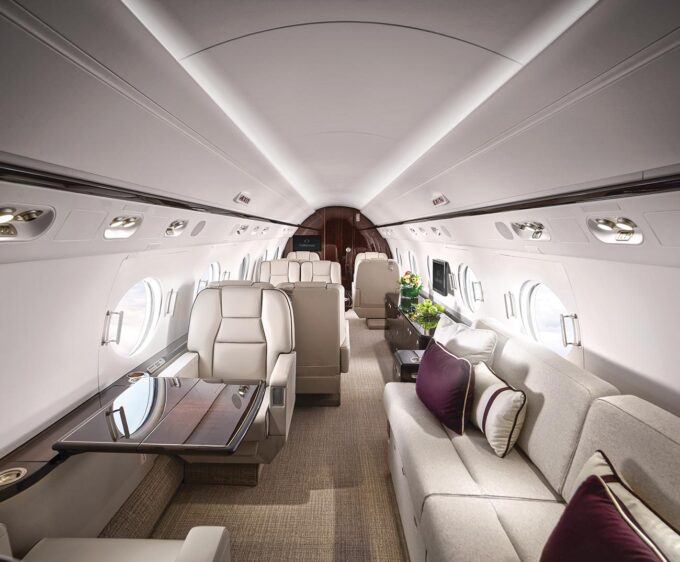 Jet Charter Interior of a luxury Private Jet Charter featuring plush seating, elegant wood accents, and ambient lighting. The cabin includes a couch, armchairs, and a polished table, exuding comfort and style. Jetvia