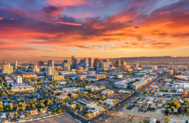 Jet Charter Aerial view of Scottsdale, Arizona cityscape during sunset, with a vivid, colorful sky and a mixture of high-rise buildings and residential areas. The distant mountains create a picturesque backdrop, enhancing the overall beauty of the urban landscape. Jetvia