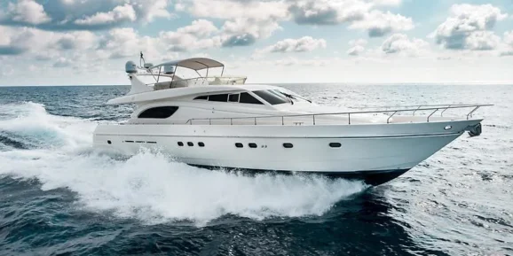 Jet Charter A sleek white luxury yacht cruises through the open ocean, cutting through the waves with speed. The sky above is partly cloudy, creating a perfect blend of blue and white over the vast expanse of water. The private yacht's polished exterior gleams under the daylight. Jetvia