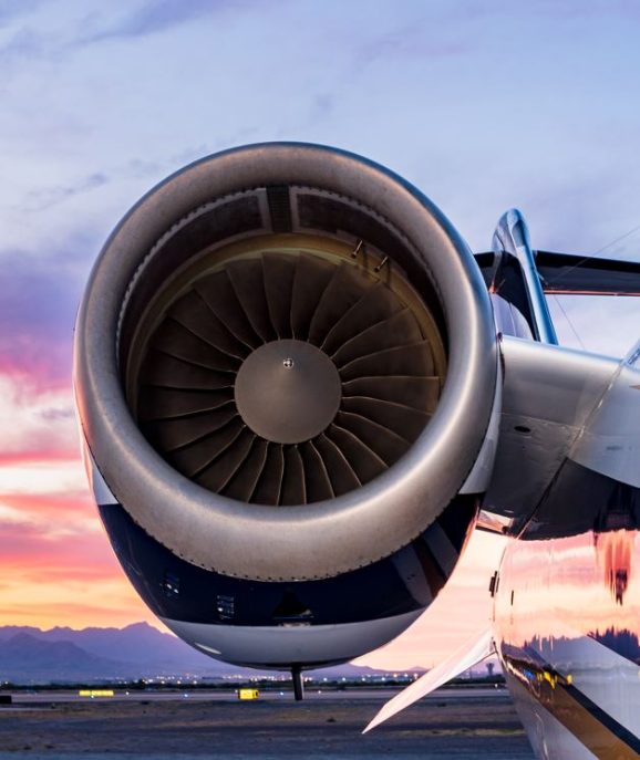 Jet Charter Close-up view of a jet engine attached to an airplane wing, with a colorful sunset sky and distant mountains in the background—a scene that inspires dreams of flight and makes you wonder what a Private Jet Cost Calculator might reveal. Jetvia