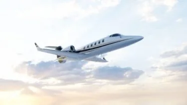 Jet Charter A sleek private jet flies through a partly cloudy sky, with sunlight illuminating the clouds and reflecting off the airplane's fuselage. Jetvia