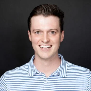 Jet Charter A smiling person with short dark hair wearing a light blue and white striped polo shirt stands in front of a plain dark background. Jetvia